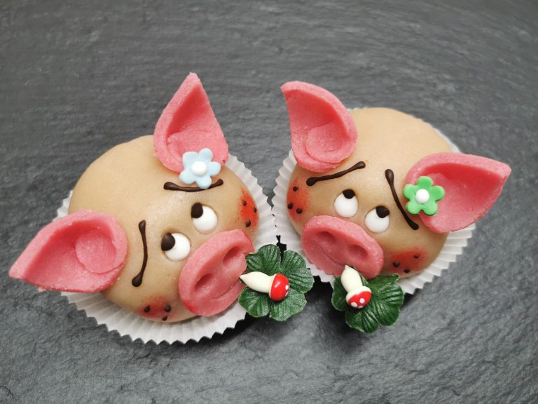Zwei niedliche, kunstvoll dekorierte Muffins in Form von Schweinen mit Blümchen.