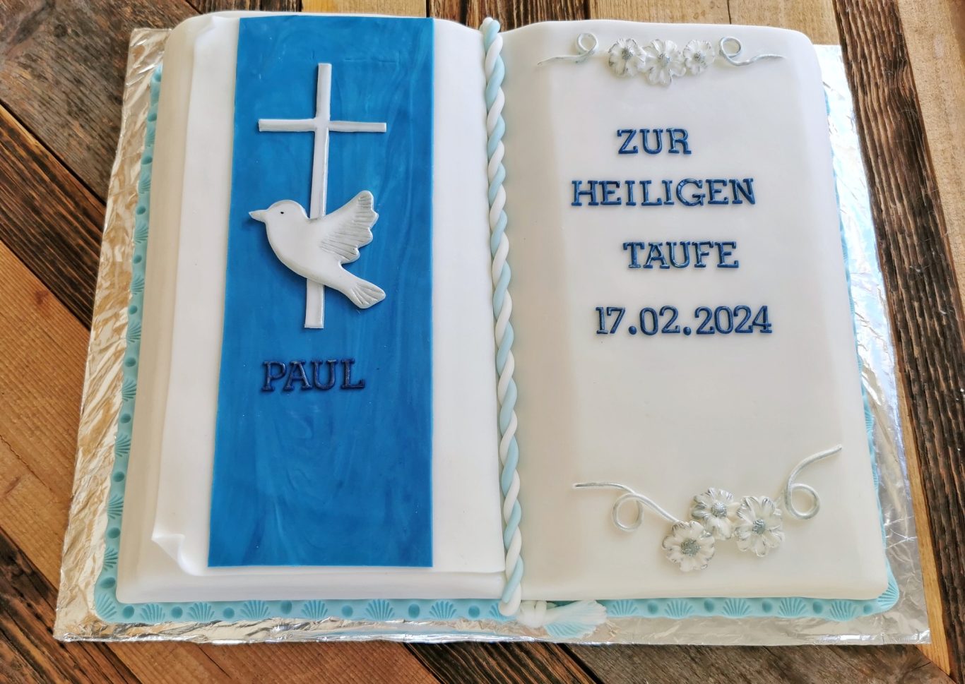 Taufkuchen in Form eines Buches mit Kreuz und Taube, beschriftet mit „Zur heiligen Taufe“.