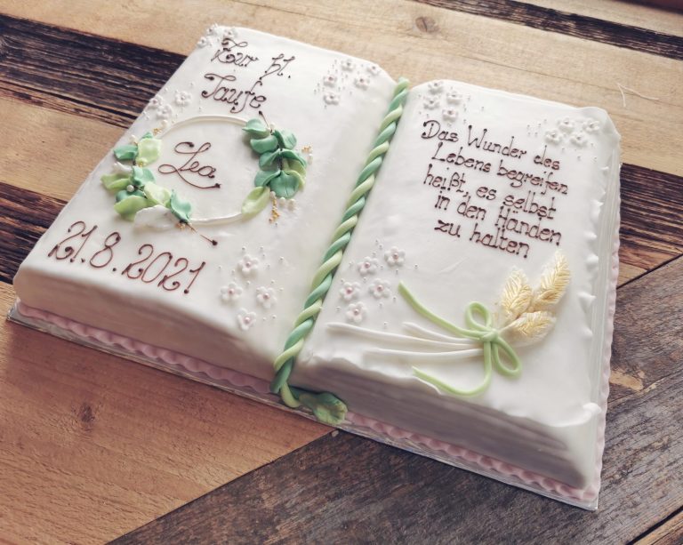 Torte in Form eines aufgeschlagenen Buches mit Blumen und Schriftzügen.