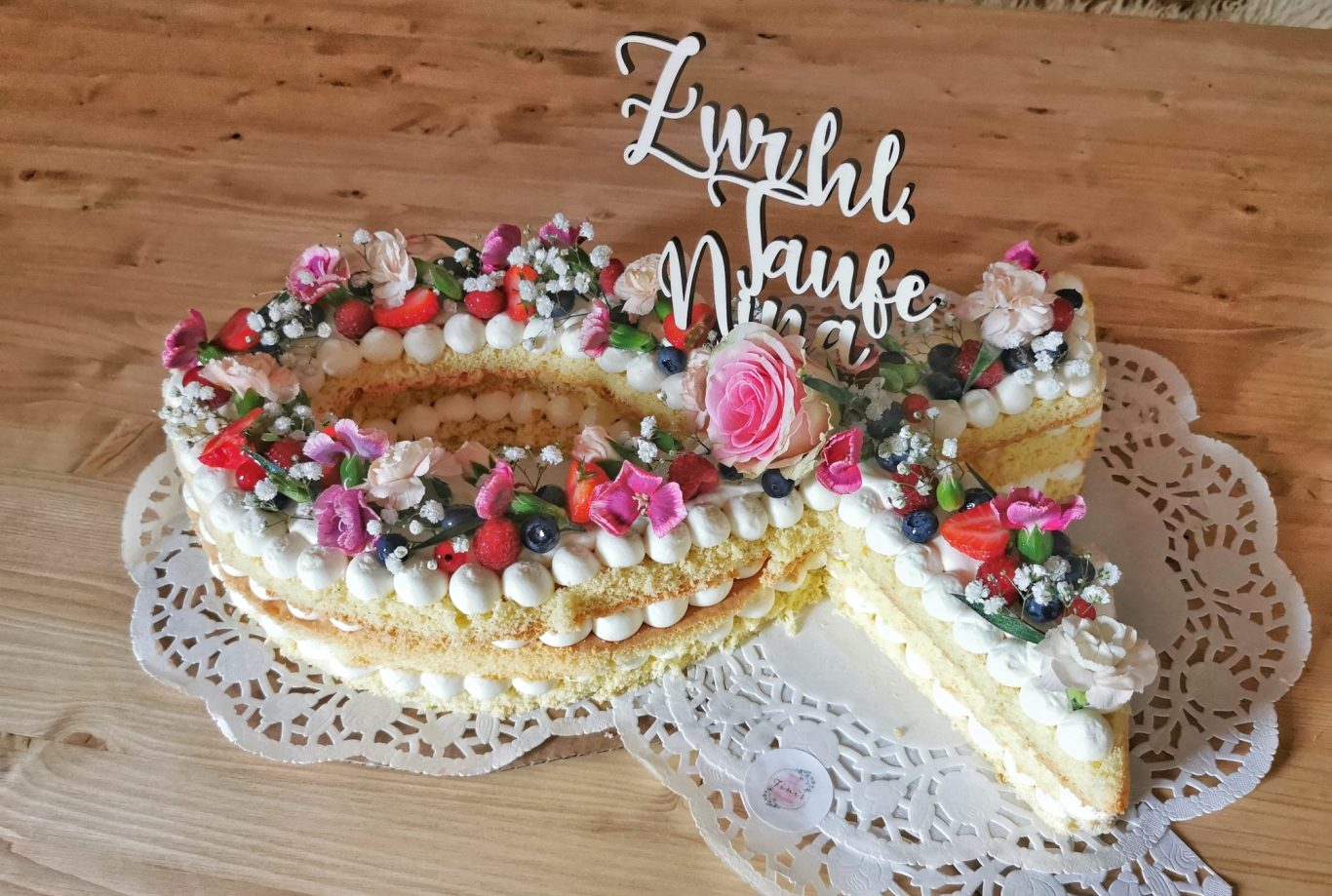 Eine große, verzierte Sahnetorte mit Blumen und Schriftzug.